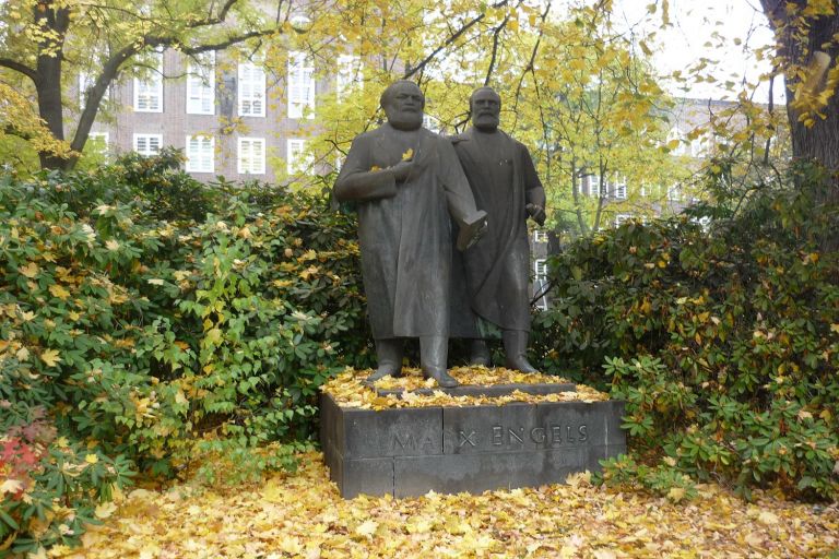 auf einem laubbedeckten Steinsockel steht die Bronzeplastik mit Marx und Engels