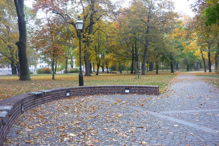 geplasterter Weg mit Laterne und einer rondellförmigen halbhohen Mauer mit Sitzgelegenheiten